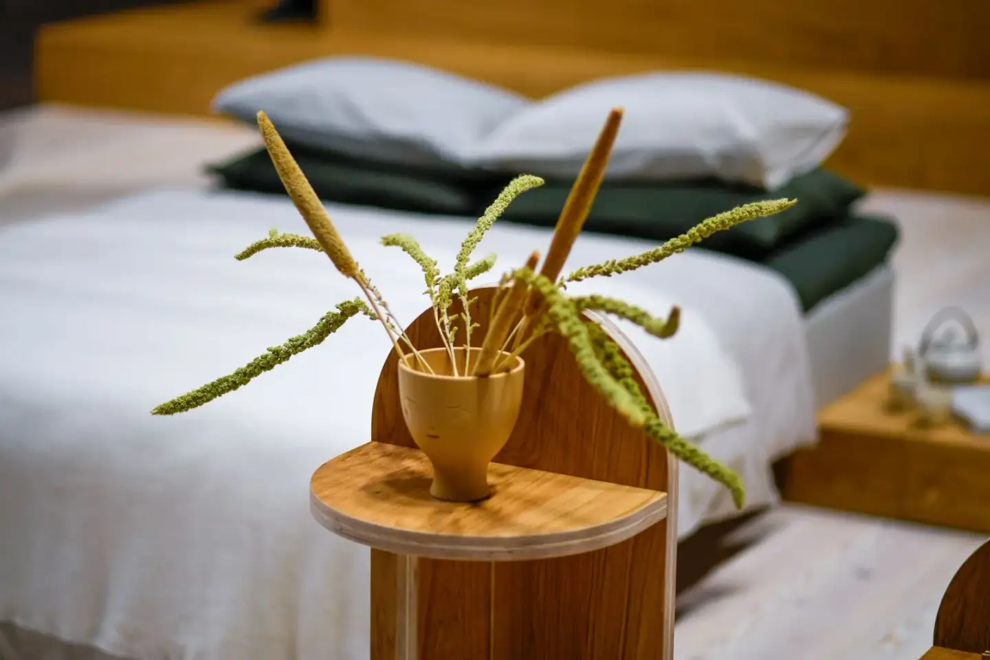 Chambre ordonnée au linge naturel, avec une petite table en bois et un vase de fleurs séchées