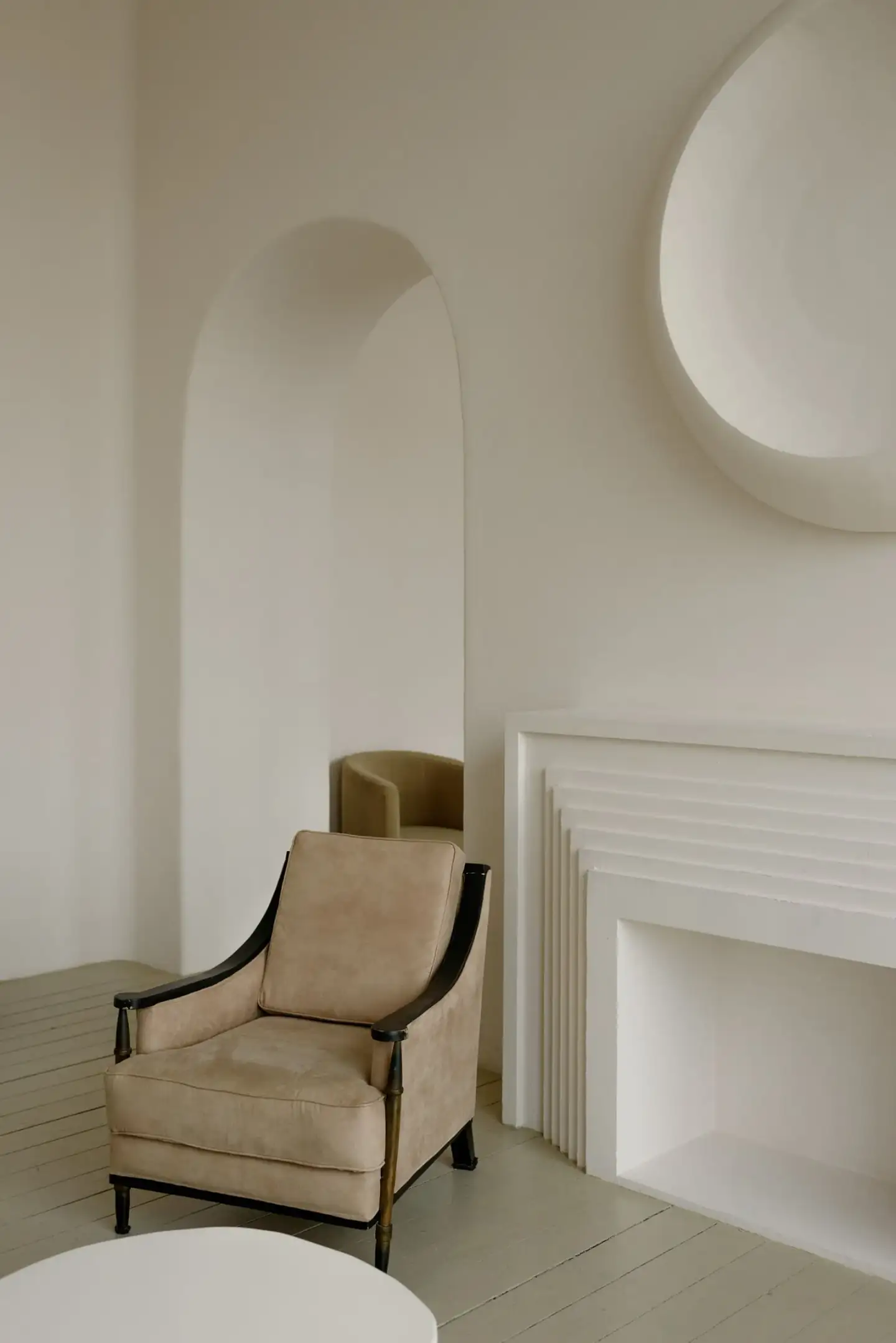 Salon épuré aux murs clairs, fauteuil beige, niche en arche et volumes largement dégagés