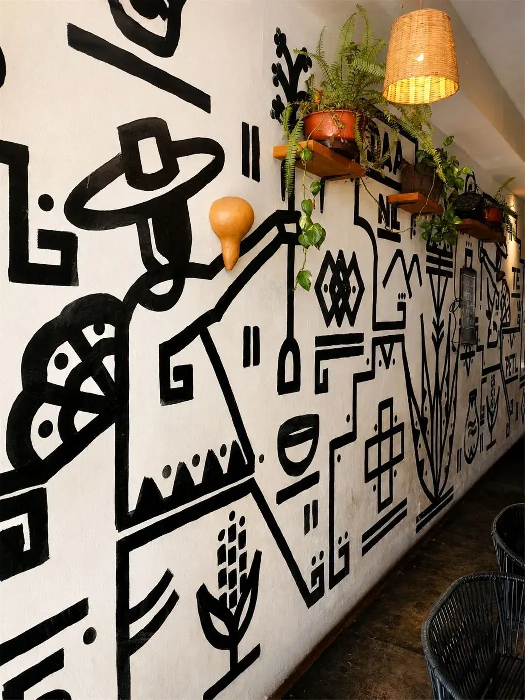 Fresque murale graphique en noir et blanc mise en valeur par des étagères en bois et des plantes suspendues à l’accueil